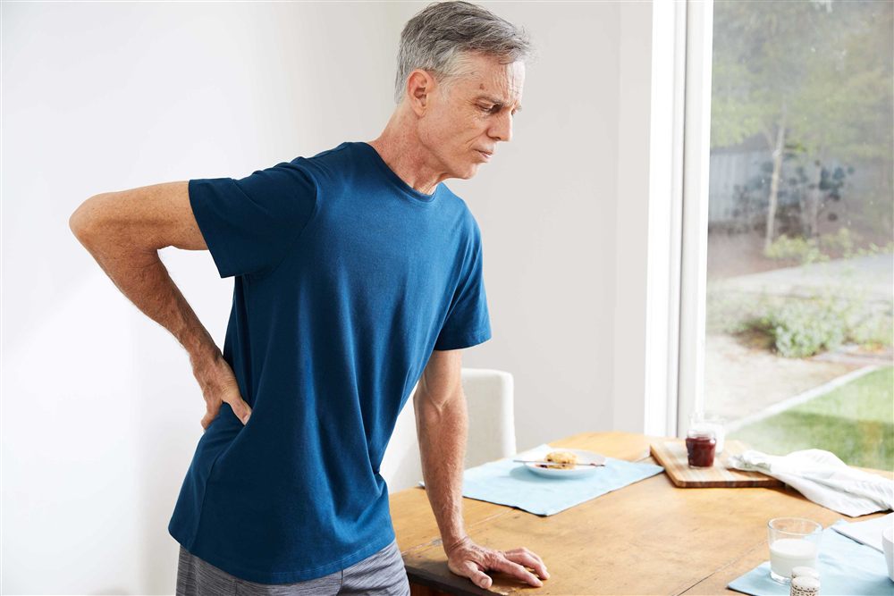 Person experiencing back discomfort at home