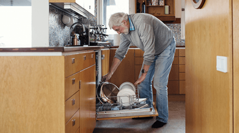 Older adult bending down to unload a lower dishwasher rack